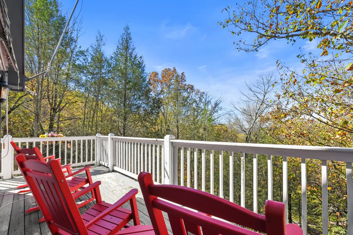 A pair of bright red rocking chairs on a welcoming wooden deck, facing out toward a view of green trees. The setting suggests a peaceful space to relax, watch sunsets, or listen to the sounds of nature after a busy day exploring the Smokies.